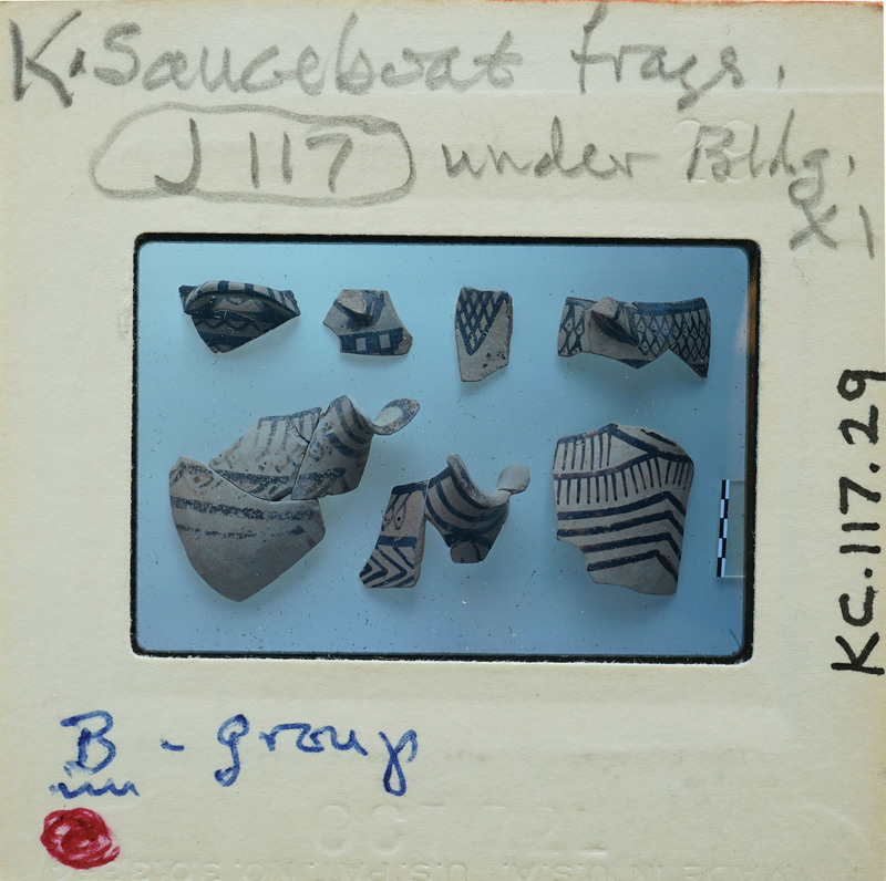 A collection of ancient Greek pottery shards on a white surface with labels and notes.
