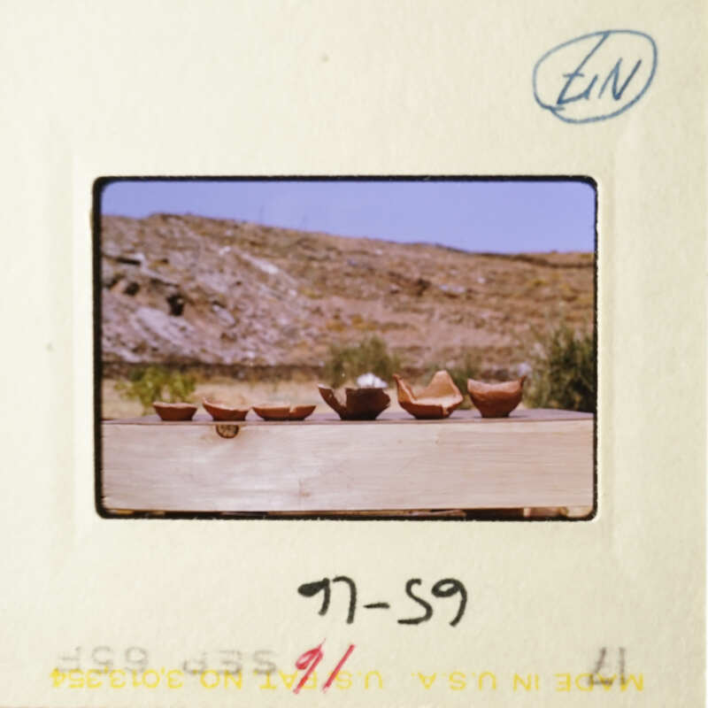 A photograph of a wooden table with four bowls on it, set against a desert landscape.