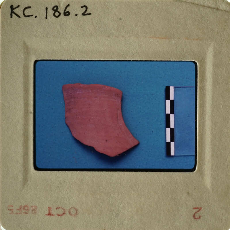 A photograph of an artifact, possibly pottery, with measurement lines and labels indicating its archaeological significance.