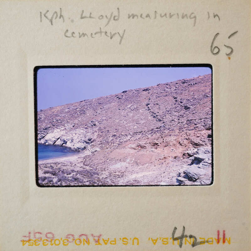 A photograph of a rocky coastline with a body of water and a hilly landscape.