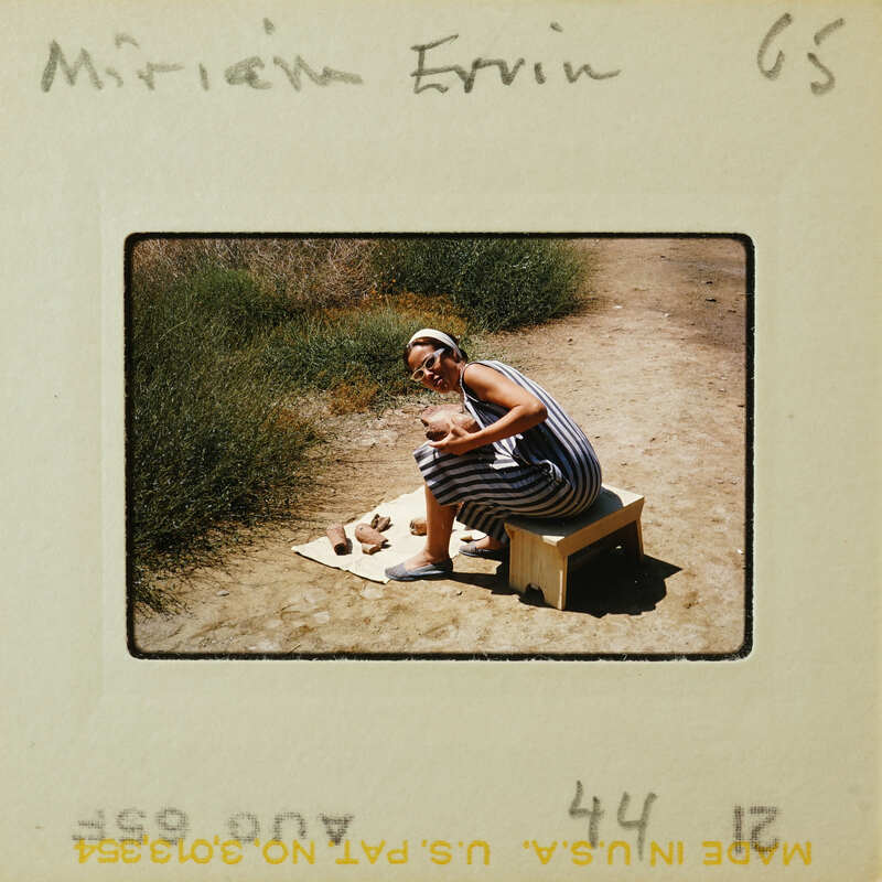 Woman sitting on a bench outdoors, holding a baby.