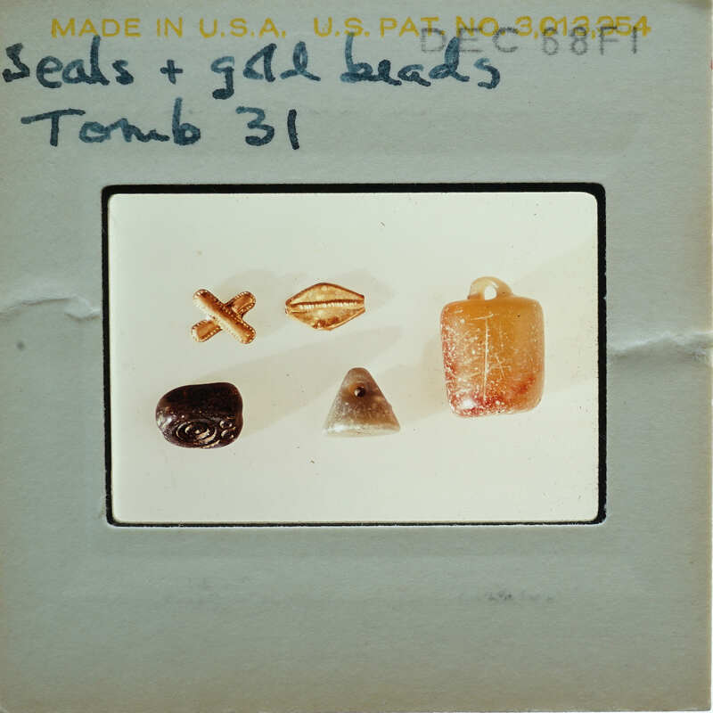A collection of small objects, including beads and stones, displayed on a white surface with labels indicating they are from "Tomb 31".