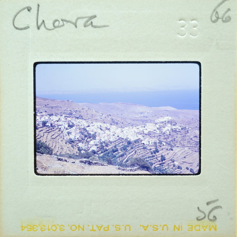 A vintage photograph of a coastal village with blue water and mountains, labeled "Chora" on the border.