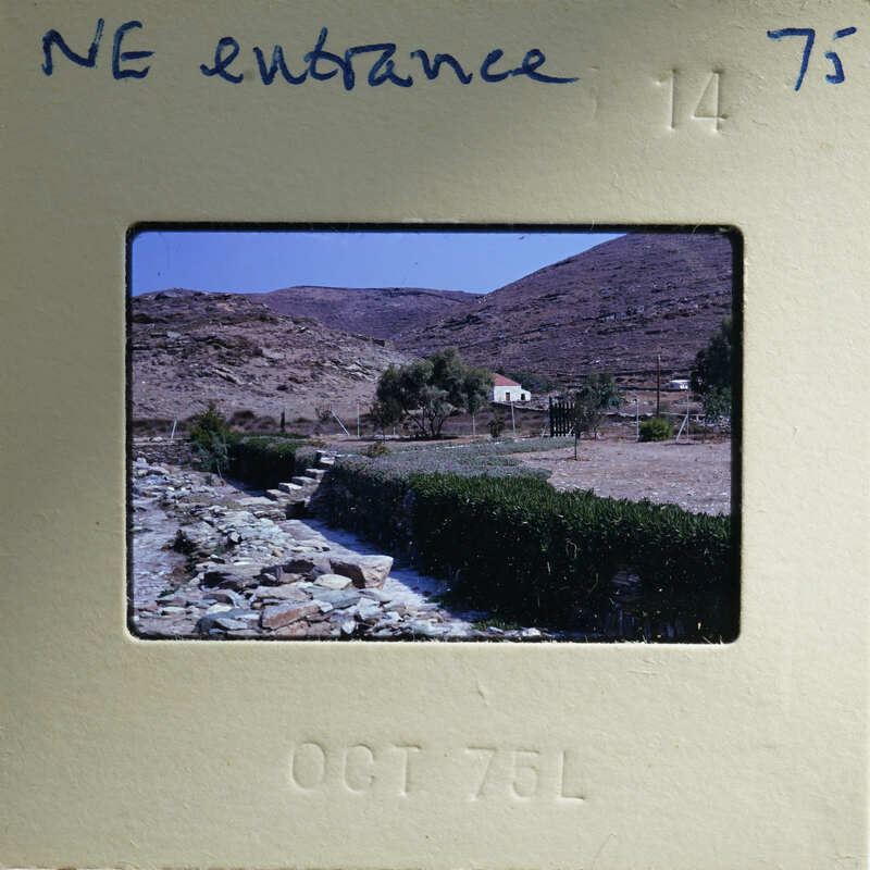 Old photograph of a rural landscape with mountains, trees, and a stone wall.