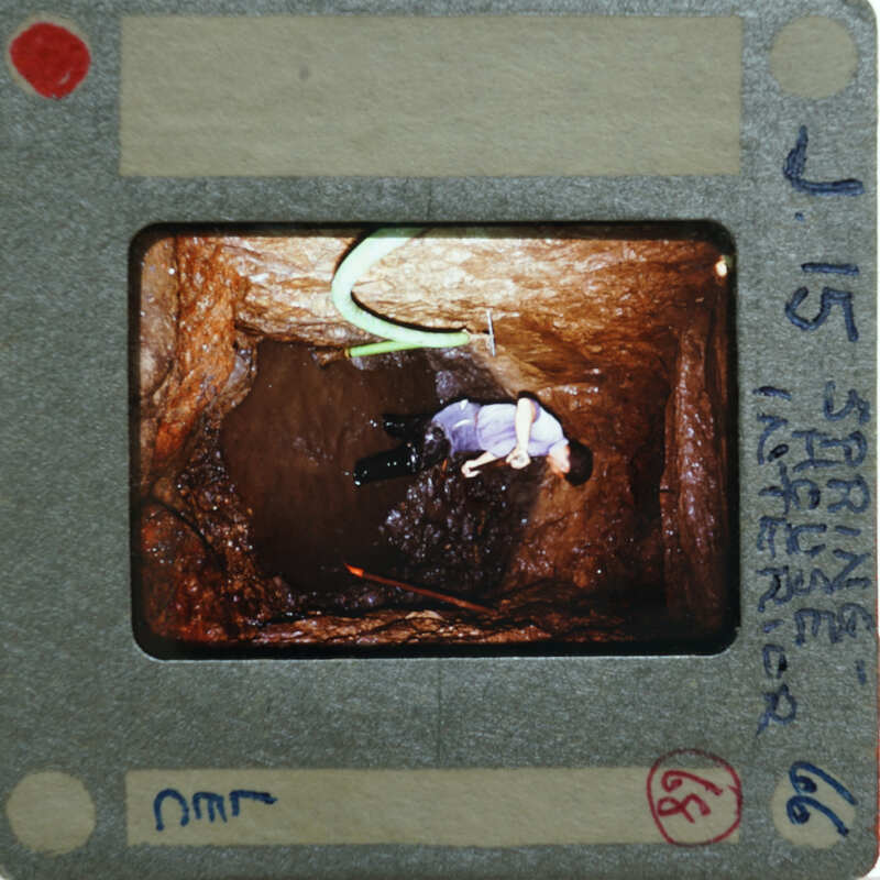 A photograph of a person inside a narrow, dark tunnel with handwritten notes on the film strip.