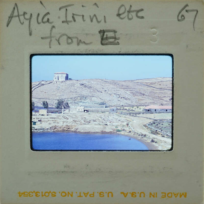 A photograph of a coastal landscape with a body of water, hills, and buildings.