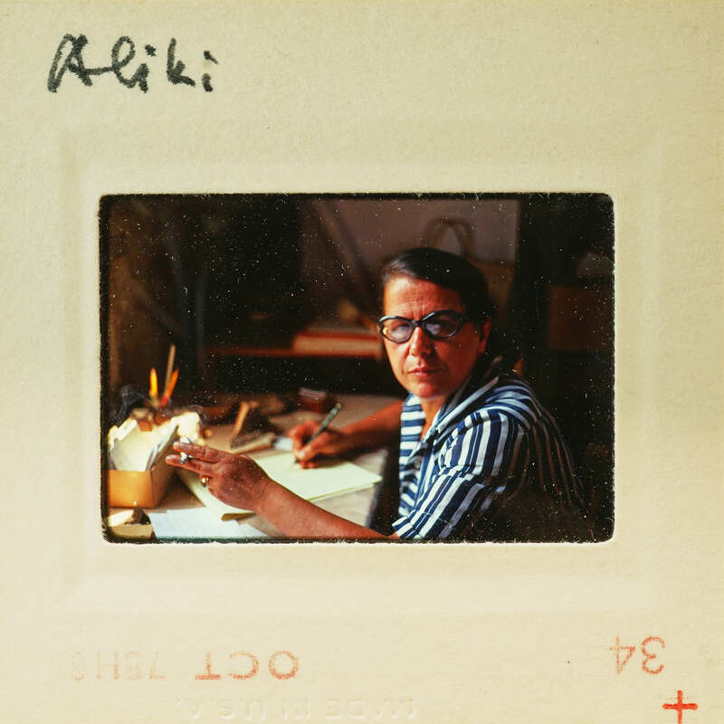 Woman wearing glasses and striped shirt, sitting at desk with papers.