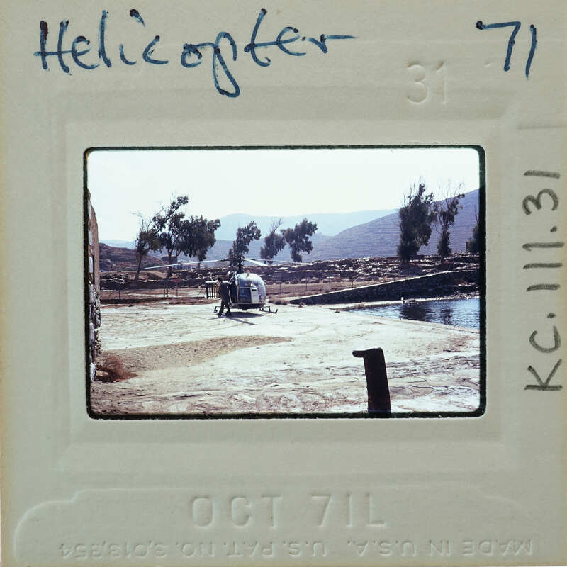 Helicopter parked on a dirt area with mountains in the background.