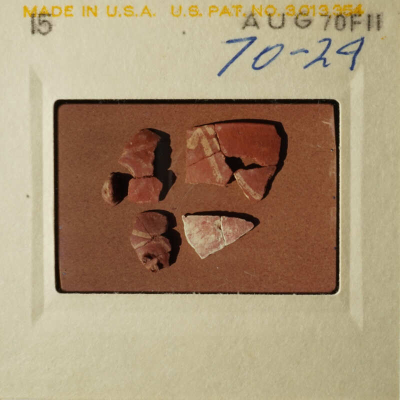 The image shows a brown paper with three red clay pottery pieces on it, placed against a light background.