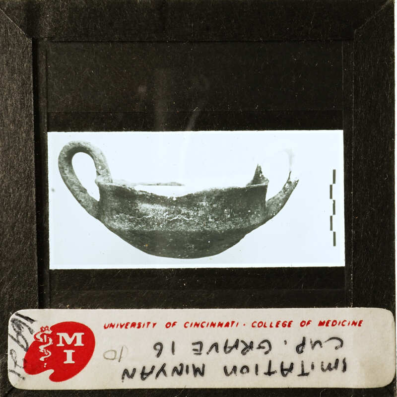 Old black and white photograph of a clay pot with visible cracks, displayed on a light box with labels and measurements.