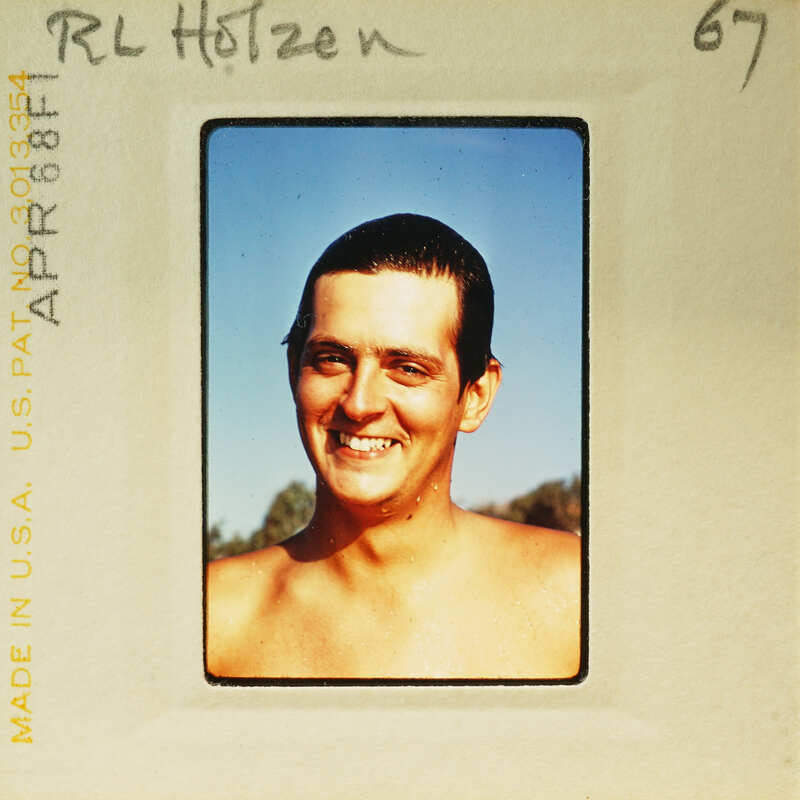 An old photograph of a smiling man with short hair, wearing no shirt.