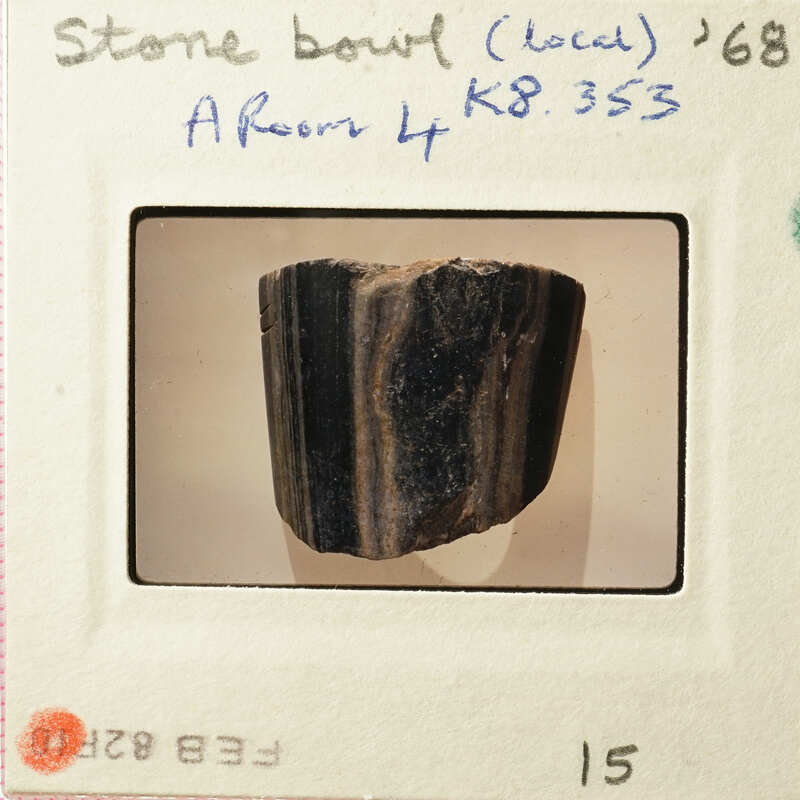 A photograph of an ancient stone bowl with visible markings and textures, displayed on a white surface.