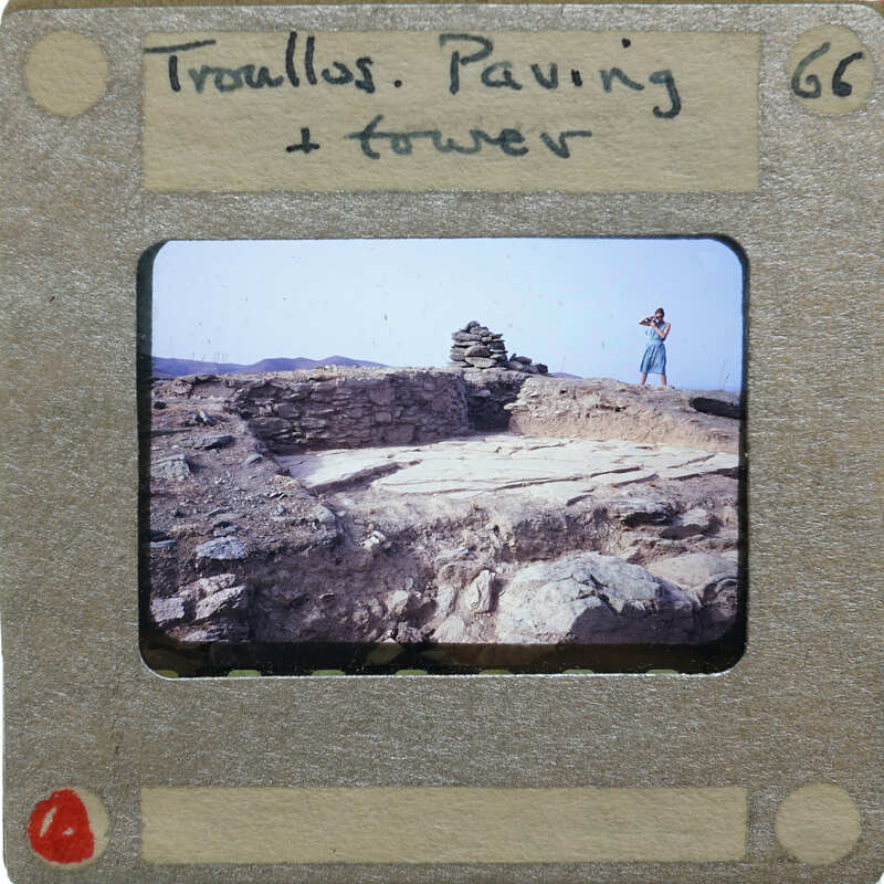 A vintage photo of a person standing near an ancient stone structure, possibly ruins or a historical site.