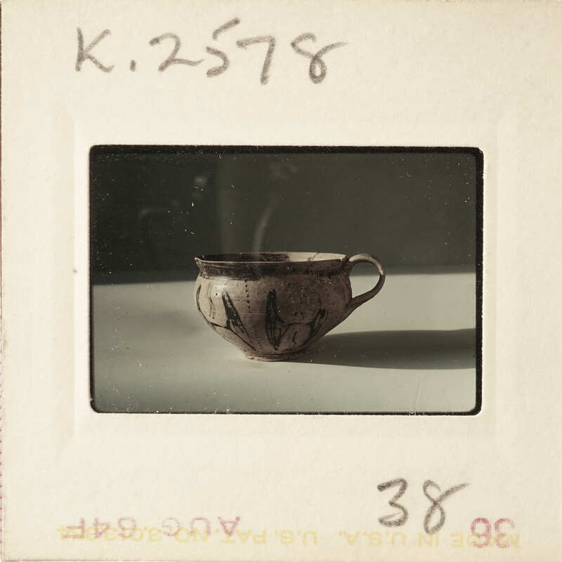 A single, old-fashioned ceramic cup with a handle on a white surface.