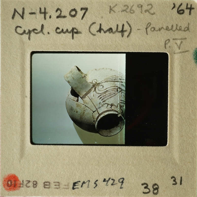 Ancient Greek vase with intricate design, photographed and labeled as "CUP HALF" on a museum card.