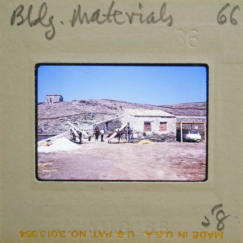 A photograph of a rustic village with stone buildings, dirt ground, and people standing around.