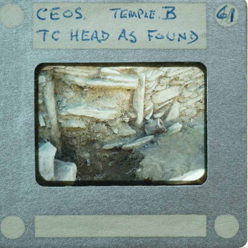 Terracotta figurine face next to stone wall.