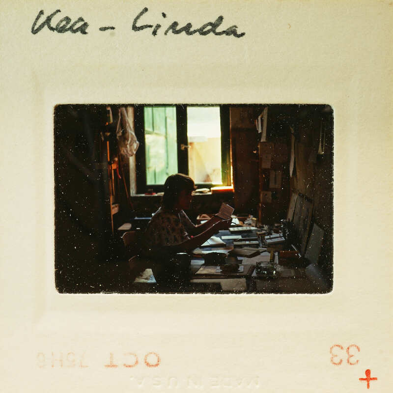 Black and white photograph of a person sitting at a desk with papers, labeled "Kea - Linda" on the border.