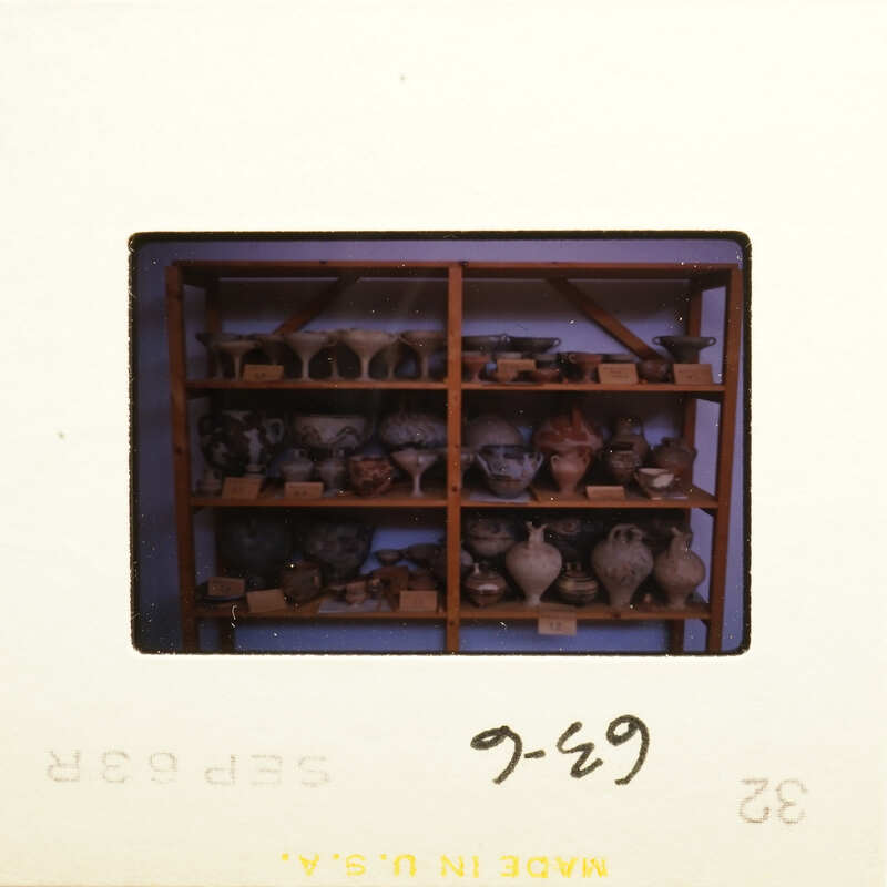 Old photograph with shelves displaying various vases and pottery.