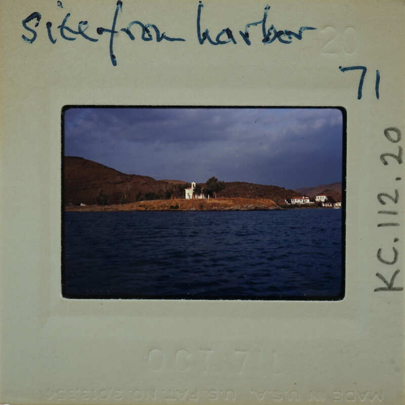 This is a photograph of a harbor with boats and houses on an island, taken from the water's edge.