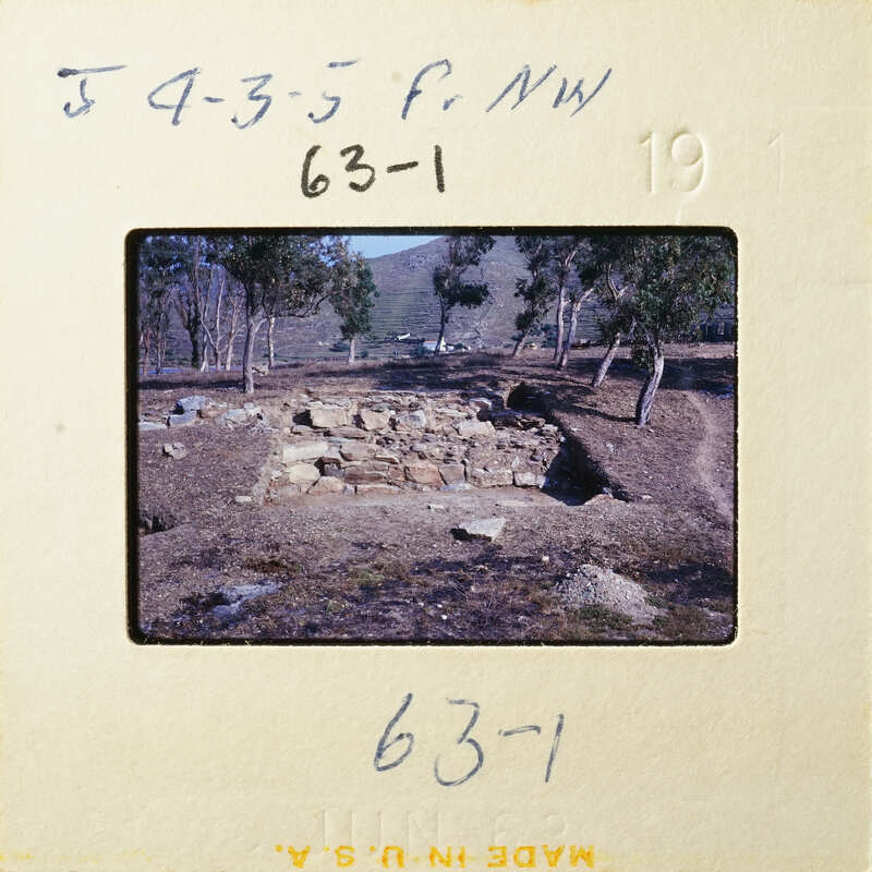 Old stone ruins with trees and mountains in the background, captured on a vintage photographic slide.