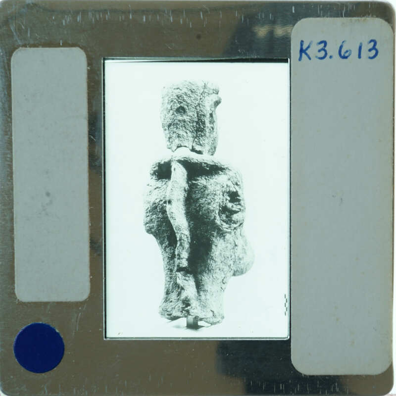 Clay figurine from behind, displayed with a white background and a label.