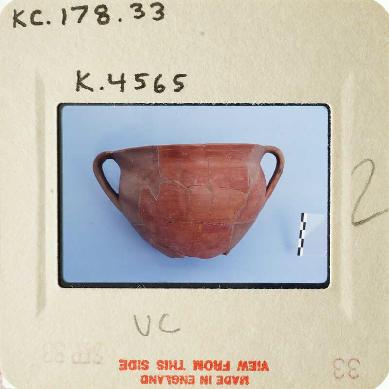 Ancient ceramic pot with visible cracks and chips, photographed on a white surface.
