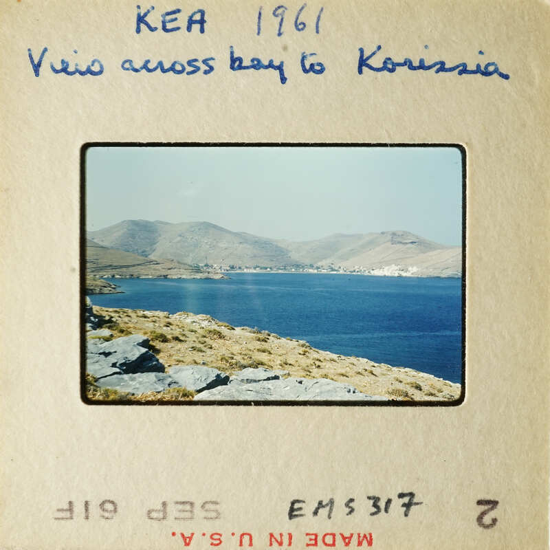 View across bay to mountains with blue water and rocky shore.