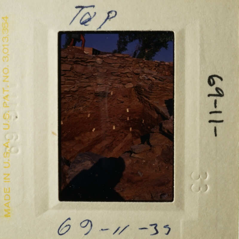 A vintage photograph in a white frame with handwritten notes, depicting a rock wall and a stone structure.