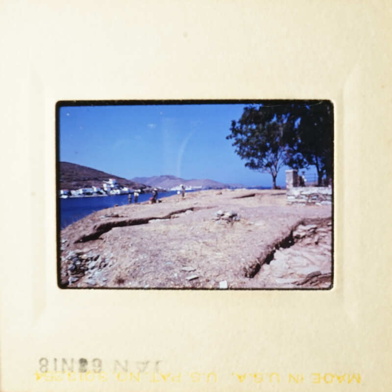 This is an old photograph of a scenic beach area with a clear sky and blue water, featuring people near the shoreline.