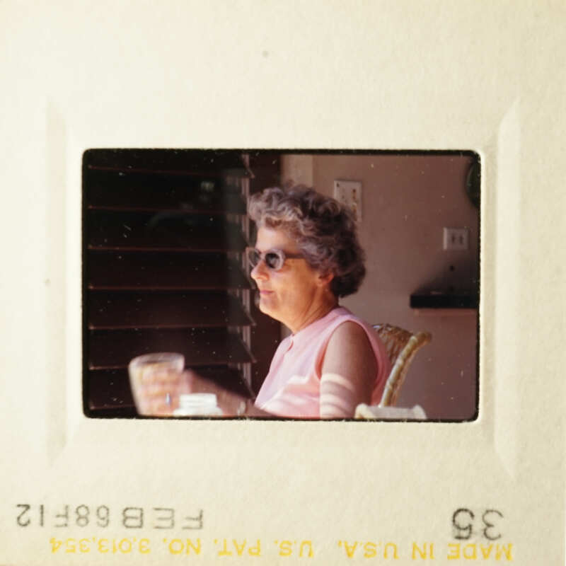 Two black and white photos of an elderly woman sitting at a table outdoors, holding a glass of water.