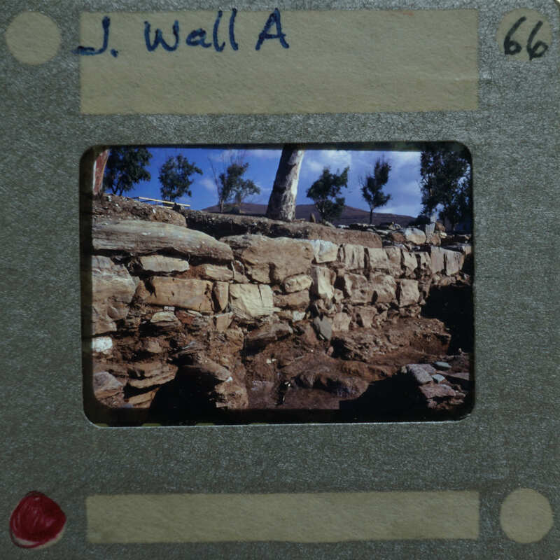 The image shows a vintage photo of an old stone wall with trees and sky in the background, framed by a film strip border.
