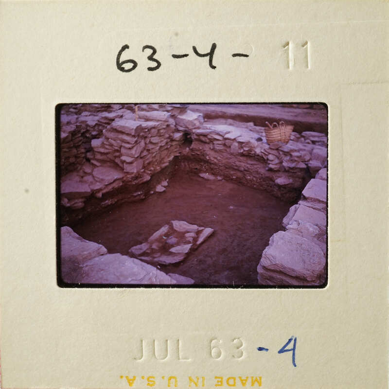 Old photograph of an archaeological site with stone ruins and a pit.