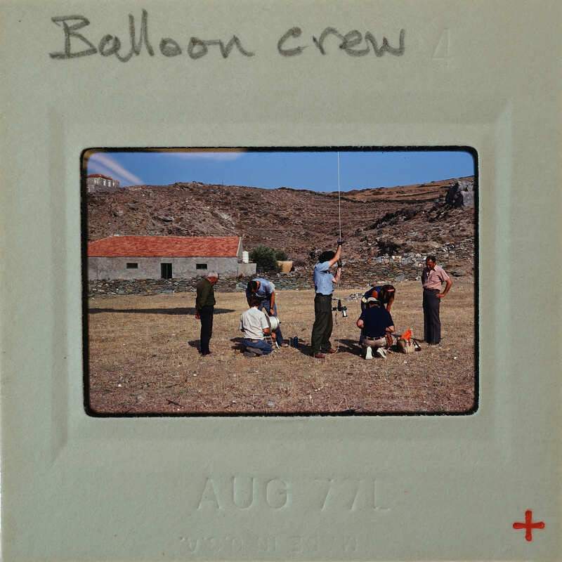 A vintage photo of a balloon crew on a rocky hillside with a blue sky background.