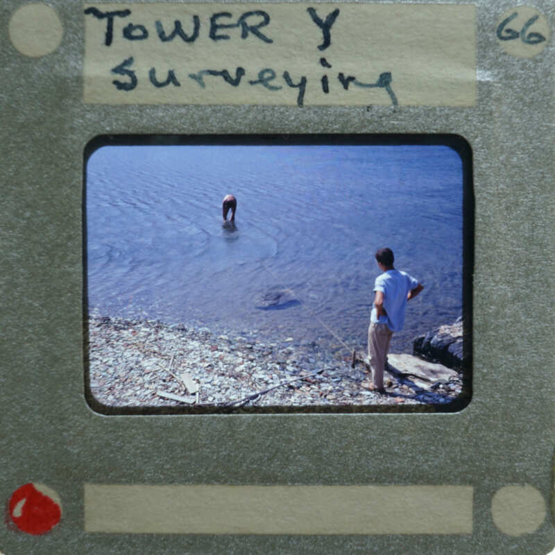 Image of a person standing on the shore while another person is wading into water, with a vintage film strip border and title "TOWER SURVEYING".