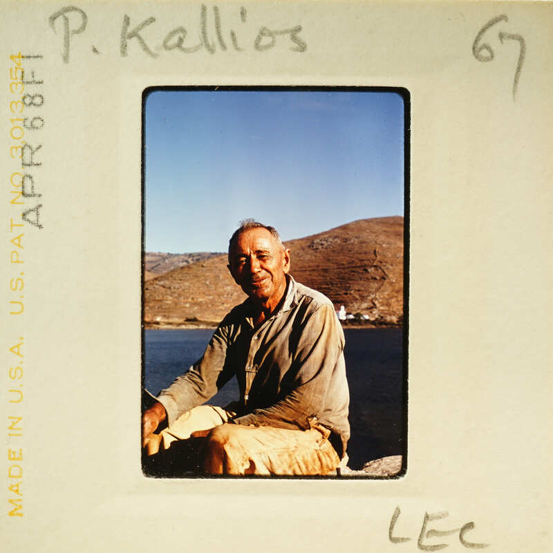 A man sitting on a rock by the water, smiling at the camera.