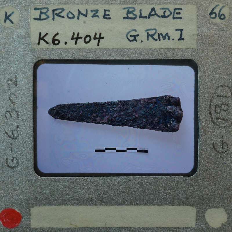 Old photograph of a bronze blade with a label and measurement marks, K6.404.