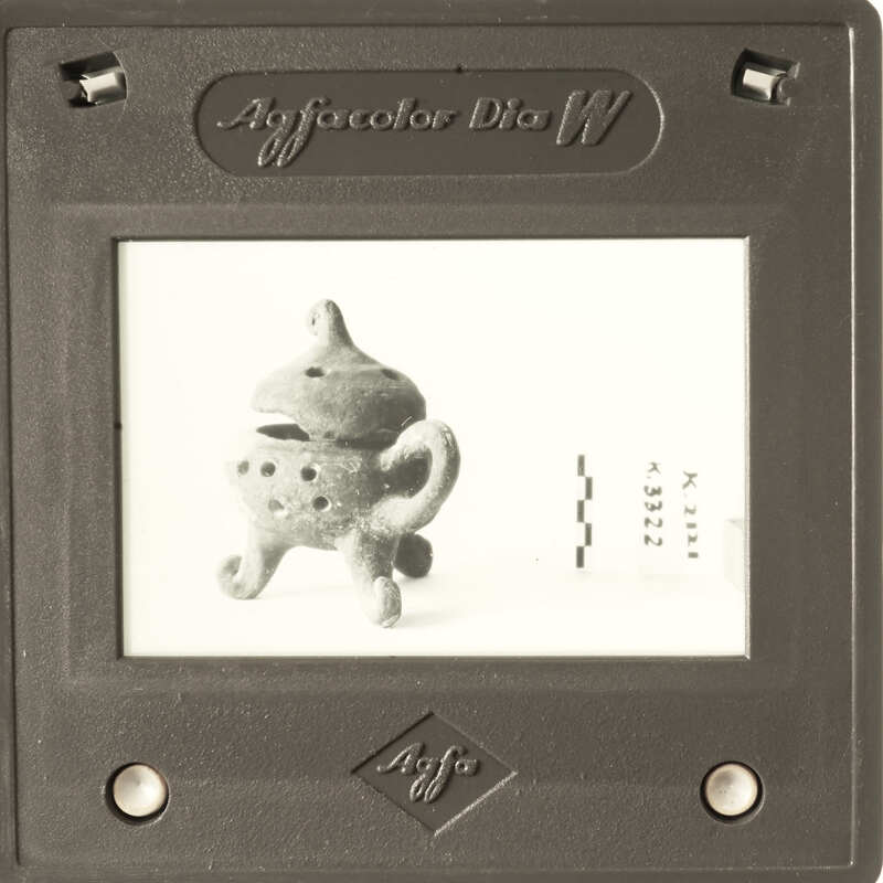 A small clay figurine of a creature with a handle on its back, displayed behind glass.