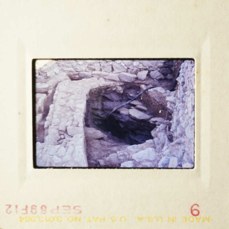 This is an image of an old photo showing a cave-like structure, possibly a sinkhole or natural feature, with a water pipe running through it.