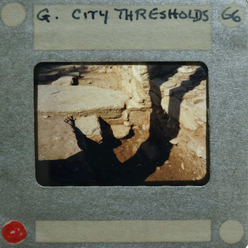 An old photograph of a historical site with visible shadows, possibly of the photographer and ruins, encased within an antique film strip holder.