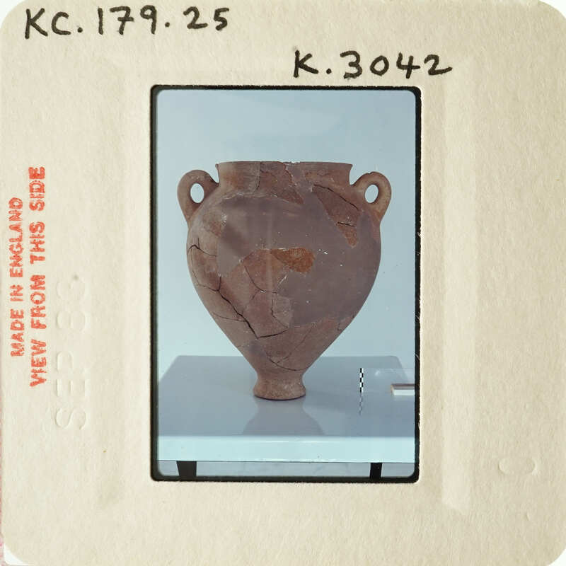 Ancient clay pot with visible cracks and chips, displayed on a stand.
