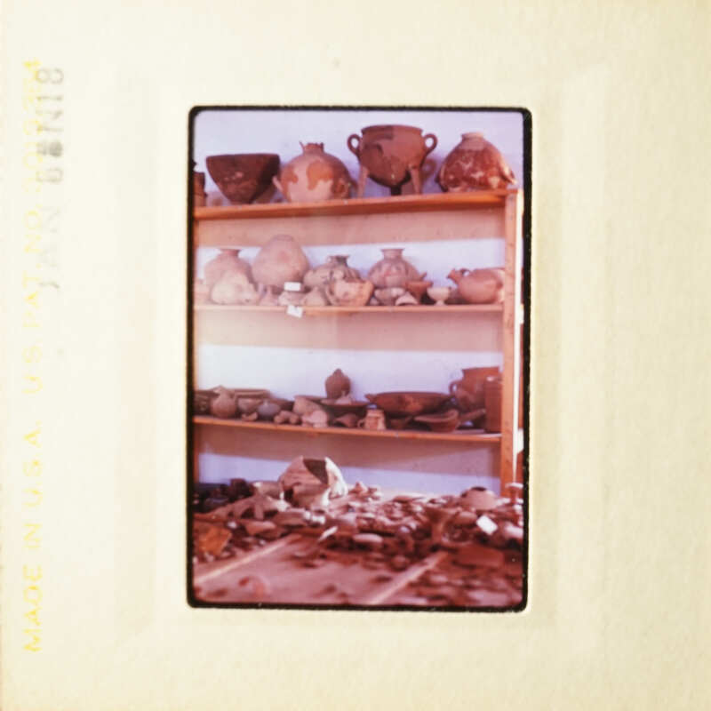 This is a photograph of an old slide showing a room filled with pottery and ceramics on shelves.