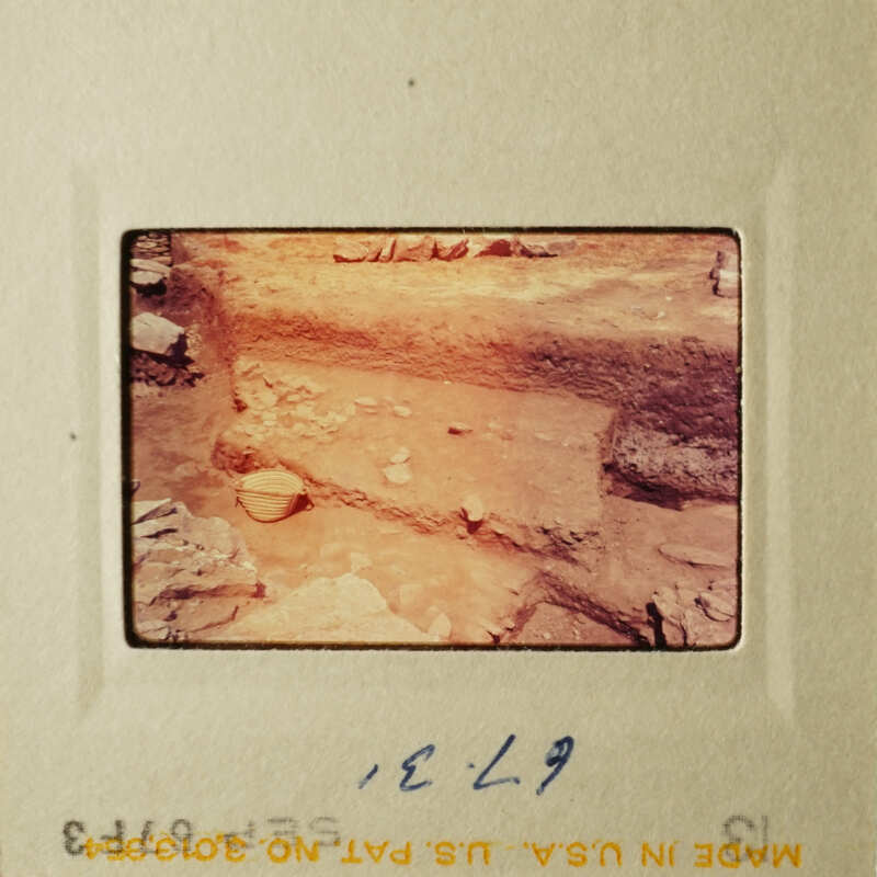 This is an old photograph of a dirt mound with rocks on top, possibly from an archaeological site.