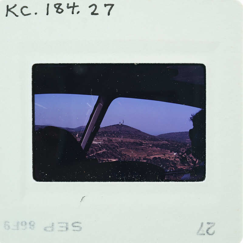 A photograph of a person sitting inside an airplane with a view of mountains outside the window.
