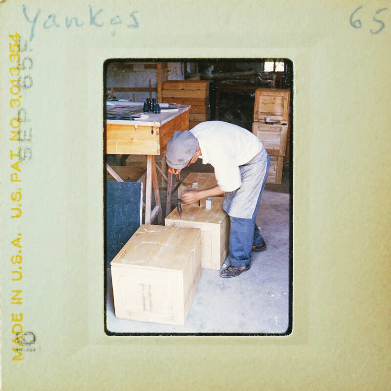 Man standing near stacked wooden crates, possibly working on them.