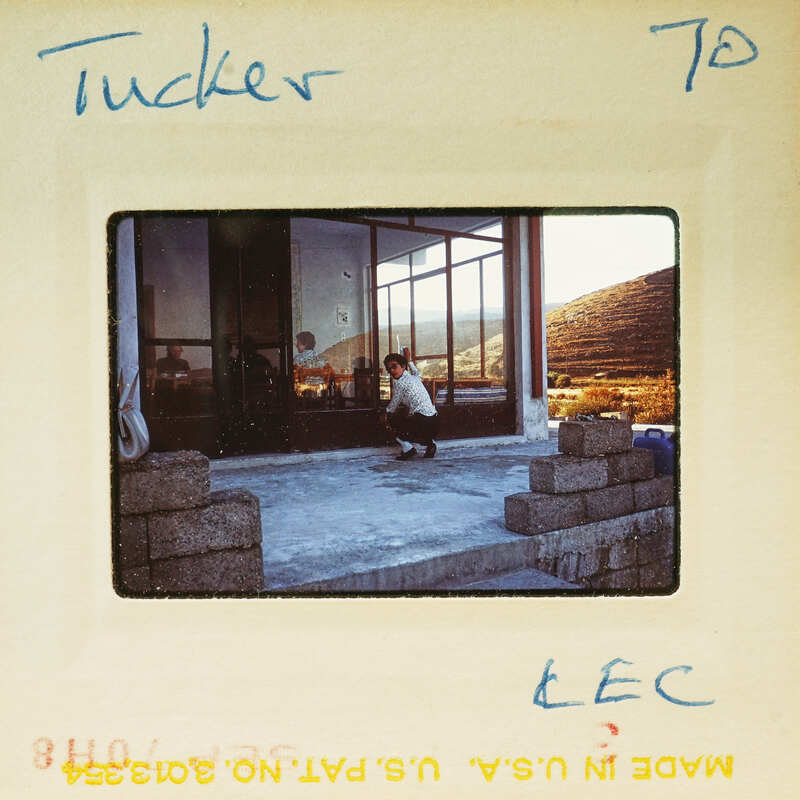 A vintage photo of a person kneeling with mountains in the background.