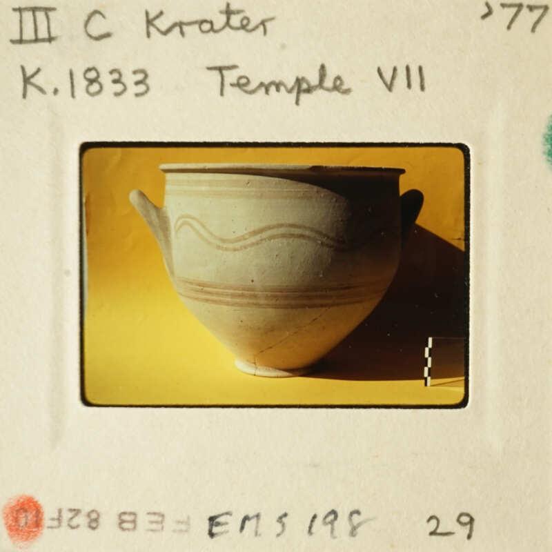 A clay pot with decorative lines on its surface, photographed against a yellow background.