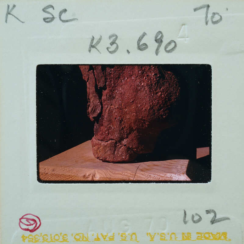 A photograph of a red clay pot with a handle, taken from above and placed on a wooden surface.