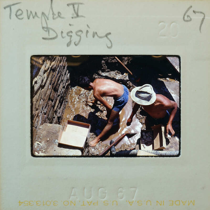 Two men excavating a muddy surface.