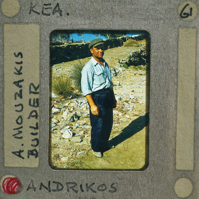 A man standing on a rocky surface with mountains in the background, captured in an old photo.